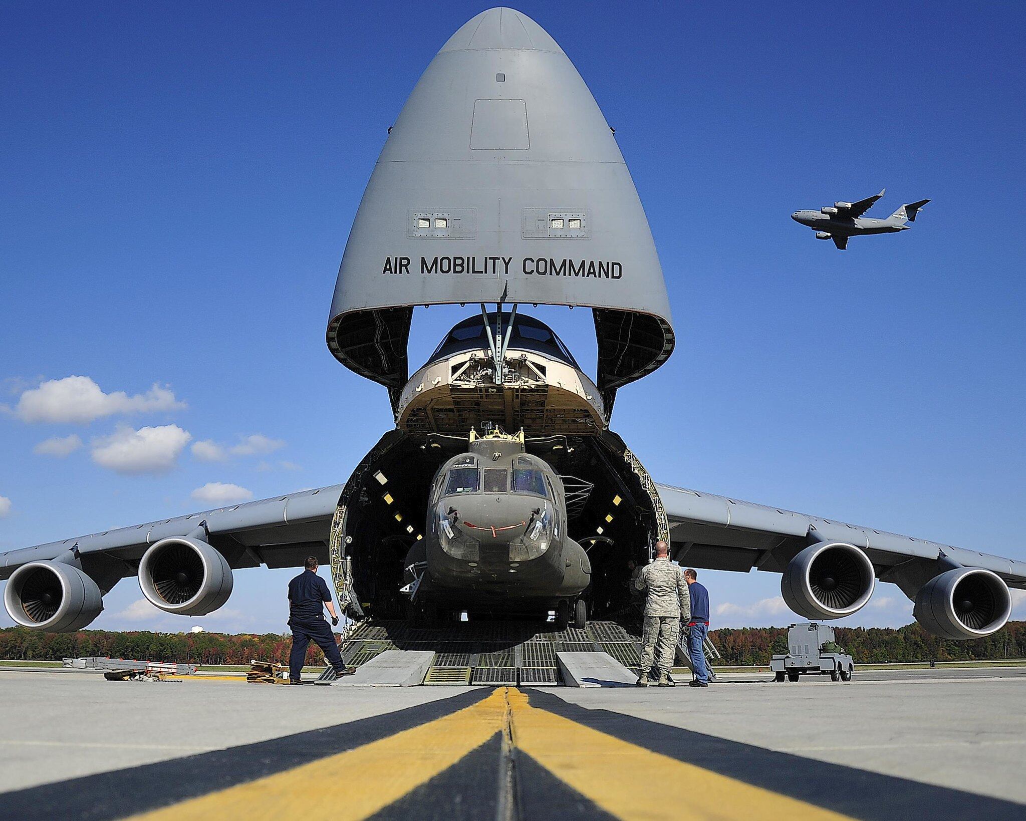 A CH-47 helicopter is unloaded from a U.S. Air Force C-5 as a C-17 takes off in the background at Westover Air Reserve Base, Mass., on Jan. 11, 2017.